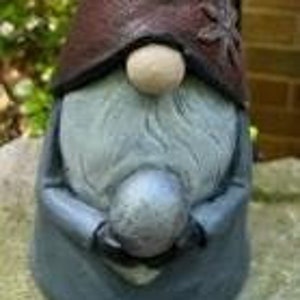 May include: A gray and red gnome figurine holding a silver ball. The gnome has a long, pointed hat with a snowflake design.