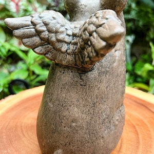 May include: A small, brown, ceramic figurine of a pig with wings. The pig is sitting on its hind legs with its wings spread out behind it.