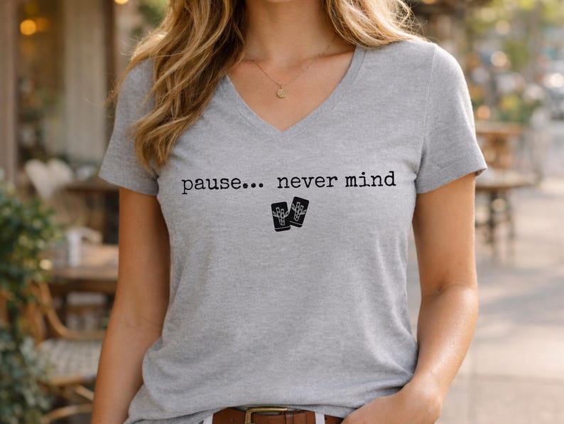 Pode incluir: Uma t-shirt cinzenta mesclada de manga curta com decote em V, apresentando o texto impresso a preto "pause... never mind" centrado no peito, acompanhado por um pequeno gr&aacute;fico de dois cart&otilde;es retangulares com uma m&atilde;o esquel&eacute;tica.