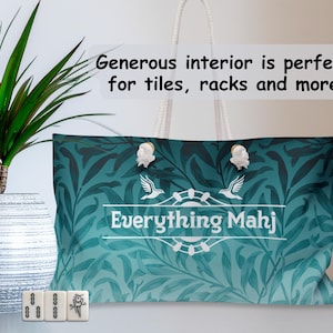 May include: Teal tote bag with a white rope handle and a floral pattern. The bag features the text "Everything Mahj" and decorative white clasps. Three Mahjong tiles are in front of the bag.