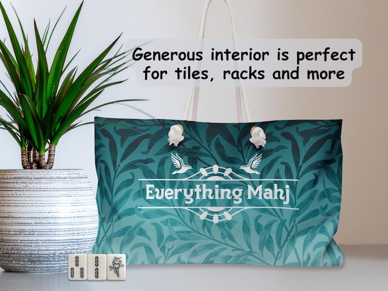 May include: Teal tote bag with a white rope handle and a floral pattern. The bag features the text "Everything Mahj" and decorative white clasps. Three Mahjong tiles are in front of the bag.