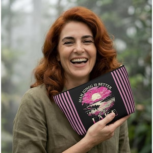 May include: Black zippered pouch with pink vertical stripes on the sides. The pouch features a graphic of a pink sun setting over a lake with the text "Mah Jongg is Better at the Lake."