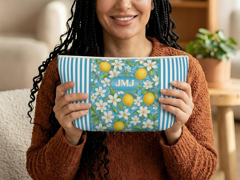 May include: A rectangular cosmetic bag with a blue and white striped pattern on the sides and a floral design in the center. The floral design features lemons, white flowers, and the initials "JMJ" in a gold frame.
