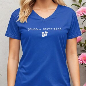Pode incluir: Uma t-shirt azul-real com decote em V apresentando o texto branco "pause... never mind" centrado no peito, acompanhado por um pequeno gr&aacute;fico de dois cart&otilde;es retangulares brancos com ilustra&ccedil;&otilde;es de cactos azuis abaixo do texto.