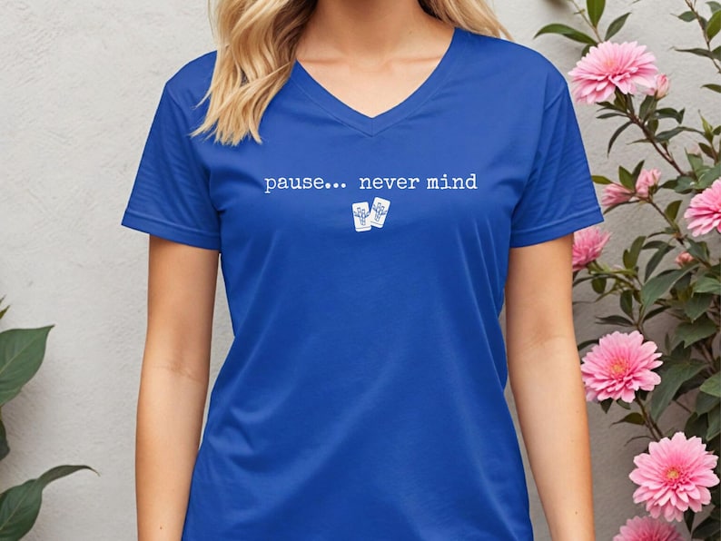 Pode incluir: Uma t-shirt azul-real com decote em V apresentando o texto branco "pause... never mind" centrado no peito, acompanhado por um pequeno gr&aacute;fico de dois cart&otilde;es retangulares brancos com ilustra&ccedil;&otilde;es de cactos azuis abaixo do texto.