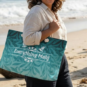 May include: A large tote bag with a teal and blue floral pattern and the text "Everything Mahj" in white. The bag has rope handles and is being held on a beach.