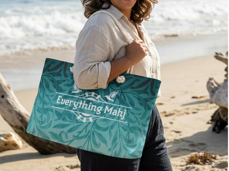 May include: A large tote bag with a teal and blue floral pattern and the text "Everything Mahj" in white. The bag has rope handles and is being held on a beach.