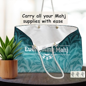 May include: A teal floral patterned tote bag with white interior, designed for Mahj supplies. It features white rope handles and text: "Carry all your Mahj supplies with ease" and "Everything Mahj". A small potted plant and Mahj tiles are on the table.