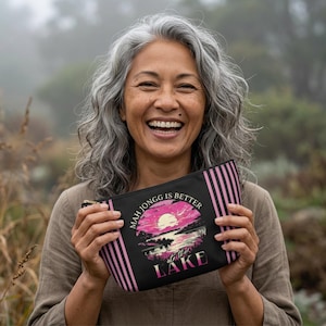 May include: Black zippered pouch with pink vertical stripes and the text "MAH JONGG IS BETTER at the LAKE" in white and pink. The pouch features a sunset scene with a pink sun, water, and trees.