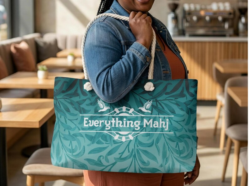 May include: A teal tote bag with a white rope handle and a floral pattern. The bag features the text "Everything Mahj" in white, with a design of two birds and a circular emblem.