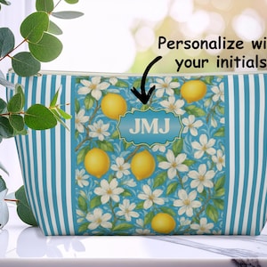 May include: A zippered cosmetic bag with a blue and white striped pattern. The center panel features a floral design with lemons and white flowers. The bag has the initials "JMJ" in a blue, decorative frame. The text "Personalize with your initials" is above the bag.