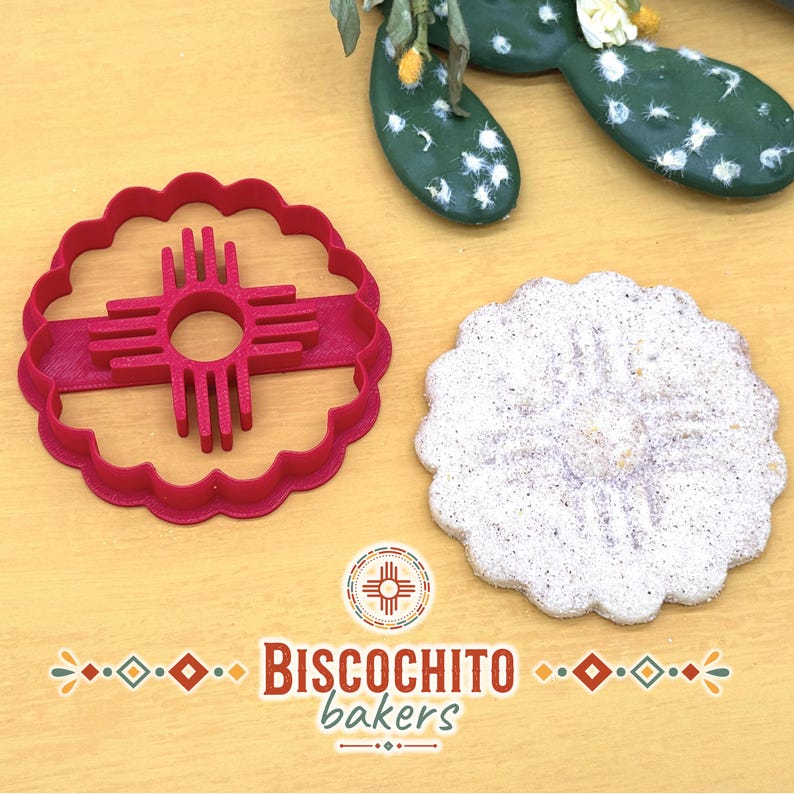 Scalloped flower biscochito cookie cutter with built-in Zia stamp beside finished Zia-imprinted cookie