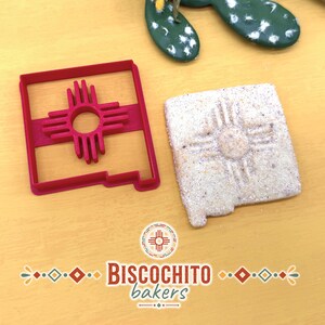 New Mexico state shaped biscochito cookie cutter with built-in Zia stamp beside finished stamped cookie