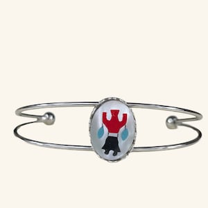 May include: A silver bangle bracelet with a white oval charm featuring a red, black, and blue Native American design.