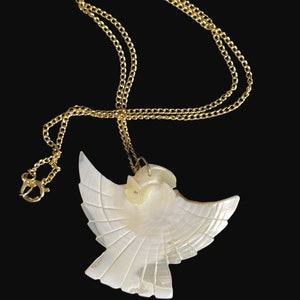 May include: A gold chain necklace with a white mother of pearl dove pendant. The dove is carved with intricate details and has a gold accent on the head.