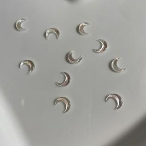 Peut inclure: Dix formes de croissant de lune en verre transparent, éparpillées sur une surface blanche.