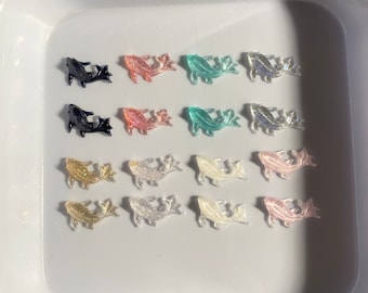 May include: A collection of 12 resin fish charms in various colors, including black, pink, blue, white, and gold. The charms are arranged in rows on a white surface.