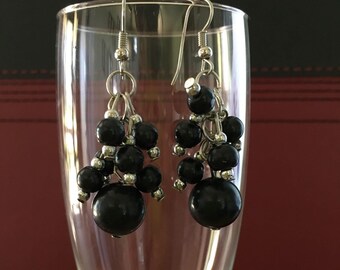 May include: A pair of dangle earrings with black beads and silver accents. The earrings are hanging from a champagne flute.