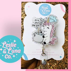 May include: A badge featuring a cartoon unicorn wearing a chef's hat, holding a pot, and the text "Came to stir the pot." The badge has a glittery border and a clear plastic backing. A teal circle with the text "Leslie & Luna Co." is also visible.