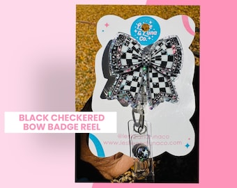 May include: Black and white checked bow badge reel with rhinestones. The bow is attached to a clear plastic badge reel with a retractable cord. The badge reel has a silver clip and a clear plastic cover. The text "Love & Luna Co." is printed on the badge reel.