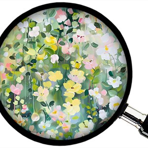 May include: A colorful floral painting viewed through a magnifying glass. The artwork features a variety of flowers in shades of yellow, pink, and white against a green background. The magnifying glass has a black frame and a silver handle.