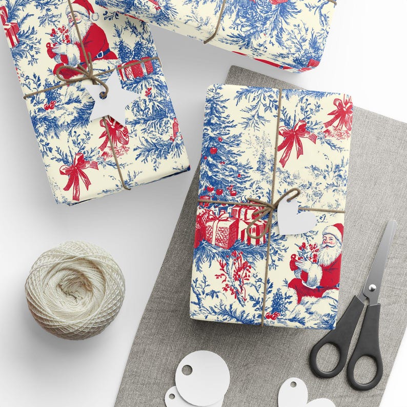 May include: Wrapping paper featuring a repeating toile pattern in red and blue on a cream background, depicting Santa Claus, Christmas trees, and gift boxes. The paper is tied with brown twine and includes white star and heart-shaped gift tags.