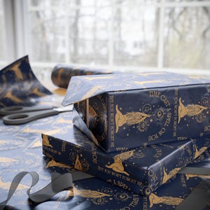 May include: Dark blue wrapping paper featuring a repeating gold-colored illustration of a person with long hair and celestial symbols. The text "TIME CAST A SPELL ON YOU BUT YOU WON'T FORGET ME" is printed in gold across the paper surface.