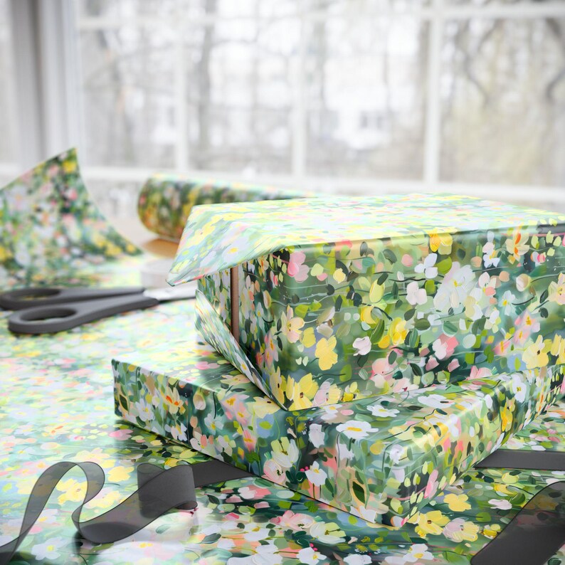 May include: Two gift boxes wrapped in floral patterned paper with yellow, pink, and white flowers on a green background. A pair of black scissors and a roll of matching wrapping paper are also visible.