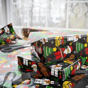 Puede incluir: Papel de regalo negro con un patr&oacute;n repetitivo de figuras tipo bloque que incluyen a Santa Claus, hombres de jengibre, mu&ntilde;ecos de nieve y &aacute;rboles de Navidad, junto con campanas y estrellas amarillas. El papel envuelve cajas rectangulares.