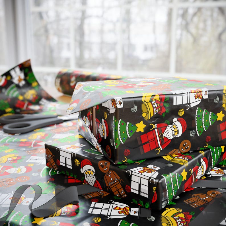 Puede incluir: Papel de regalo negro con un patr&oacute;n repetitivo de figuras tipo bloque que incluyen a Santa Claus, hombres de jengibre, mu&ntilde;ecos de nieve y &aacute;rboles de Navidad, junto con campanas y estrellas amarillas. El papel envuelve cajas rectangulares.