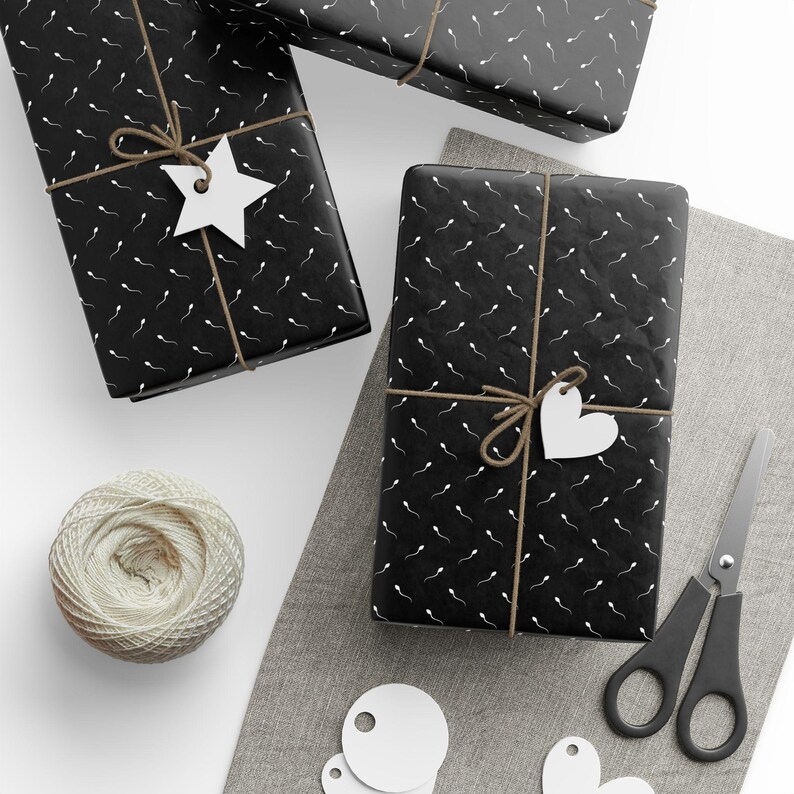 Puede incluir: Cajas de regalo rectangulares envueltas en papel negro con un patr&oacute;n repetitivo de espermatozoides blancos, atadas con cordel marr&oacute;n. Cada caja presenta una etiqueta de regalo de papel blanco en forma de estrella o coraz&oacute;n.