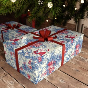 May include: Two rectangular gift boxes wrapped in cream-colored paper featuring a blue toile-style pattern of pine branches and red illustrations of Santa Claus. Each box is tied with a smooth, dark red satin ribbon arranged in a cross pattern.
