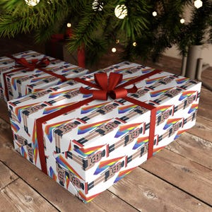 May include: Wrapping paper featuring a repeating pattern of nutcracker figures wearing black outfits and hats, each accompanied by a rainbow-colored flag. The paper is tied with a dark red ribbon bow, creating a festive presentation for gifts.