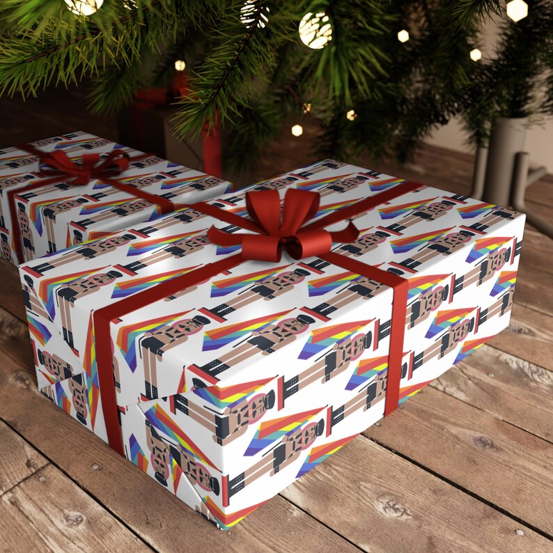 May include: Wrapping paper featuring a repeating pattern of nutcracker figures wearing black outfits and hats, each accompanied by a rainbow-colored flag. The paper is tied with a dark red ribbon bow, creating a festive presentation for gifts.