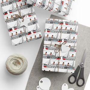 K&ouml;nnte beinhalten: Geschenke, verpackt mit einem sich wiederholenden Muster aus schwarzen, roten und orangefarbenen Schiffen auf wei&szlig;em Papier. Die Geschenke sind mit Bindfaden gebunden und mit wei&szlig;en Anh&auml;ngern versehen. Ein Kn&auml;uel Bindfaden, eine Schere und zus&auml;tzliche Anh&auml;nger sind ebenfalls zu sehen.