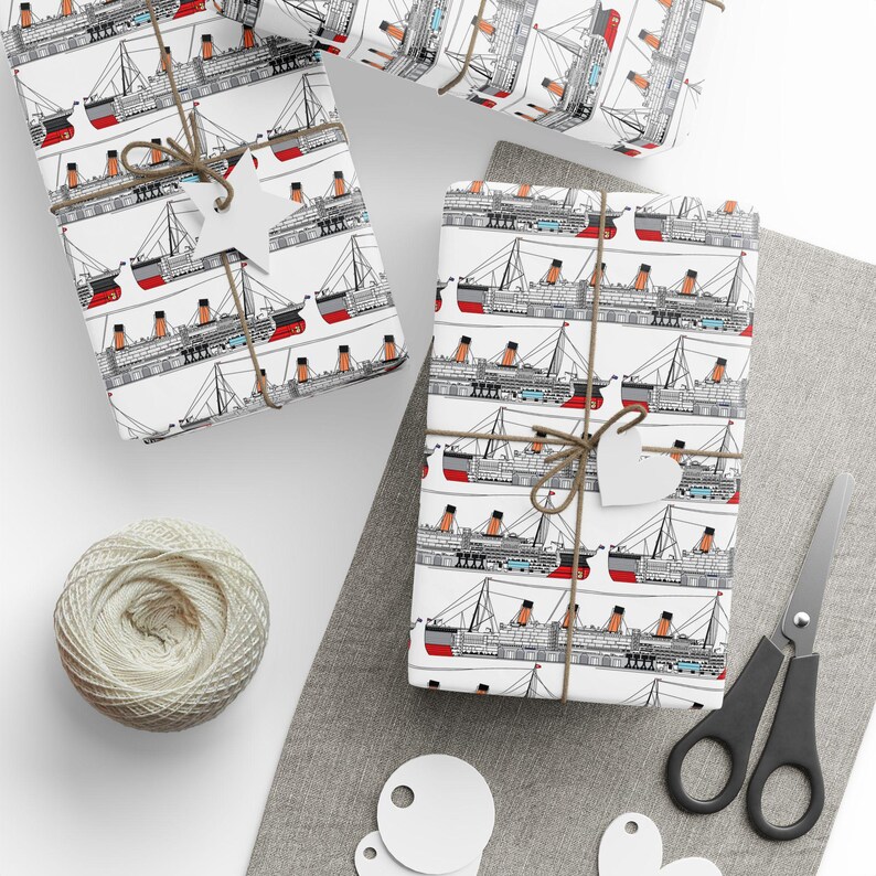 K&ouml;nnte beinhalten: Geschenke, verpackt mit einem sich wiederholenden Muster aus schwarzen, roten und orangefarbenen Schiffen auf wei&szlig;em Papier. Die Geschenke sind mit Bindfaden gebunden und mit wei&szlig;en Anh&auml;ngern versehen. Ein Kn&auml;uel Bindfaden, eine Schere und zus&auml;tzliche Anh&auml;nger sind ebenfalls zu sehen.