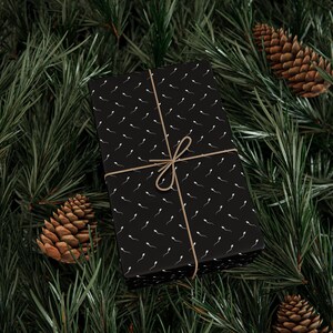 Puede incluir: Una caja de regalo rectangular envuelta en papel negro con un patr&oacute;n blanco repetitivo de espermatozoides. La caja est&aacute; atada con un cordel fino de color marr&oacute;n claro dispuesto en un patr&oacute;n de cruz simple con un peque&ntilde;o lazo en la parte superior.