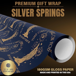 May include: A roll of dark blue gift wrap paper featuring a repeating gold-colored graphic pattern of stylized figures, eyes, and the text "TIME CAST A SPELL ON YOU BUT YOU WON'T FORGET ME". The paper is 180gsm gloss paper with a smooth finish.
