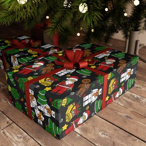 Puede incluir: Dos cajas de regalo rectangulares envueltas en papel negro con un patr&oacute;n repetitivo de figuras de dibujos animados que incluyen a Santa Claus, hombres de jengibre, mu&ntilde;ecos de nieve, &aacute;rboles de Navidad y campanas doradas, atadas con una cinta roja.