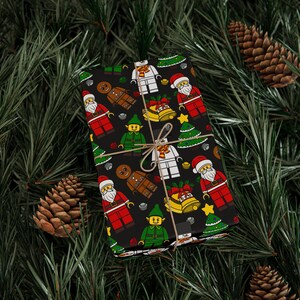 Puede incluir: Una caja de regalo rectangular envuelta en papel negro con un patr&oacute;n repetitivo de figuras de dibujos animados que incluyen a Santa Claus, elfos, hombres de jengibre, mu&ntilde;ecos de nieve, &aacute;rboles de Navidad y campanas doradas, atada con cordel marr&oacute;n.