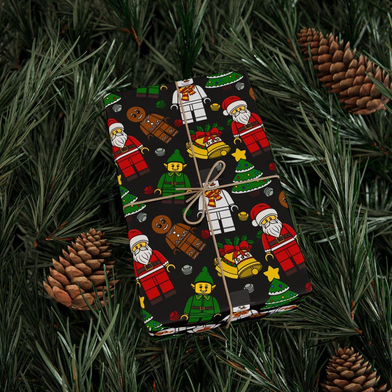 Puede incluir: Una caja de regalo rectangular envuelta en papel negro con un patr&oacute;n repetitivo de figuras de dibujos animados que incluyen a Santa Claus, elfos, hombres de jengibre, mu&ntilde;ecos de nieve, &aacute;rboles de Navidad y campanas doradas, atada con cordel marr&oacute;n.