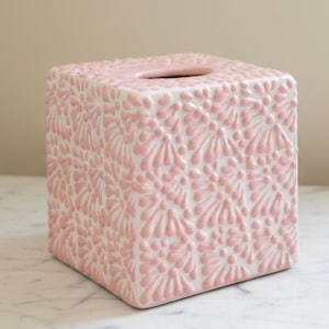 Op de afbeelding: Vierkante, roze tissuebox met een verhoogd bloemmotief. De box is gemaakt van keramiek en staat op een wit marmeren oppervlak. De tissue-opening is ovaal.