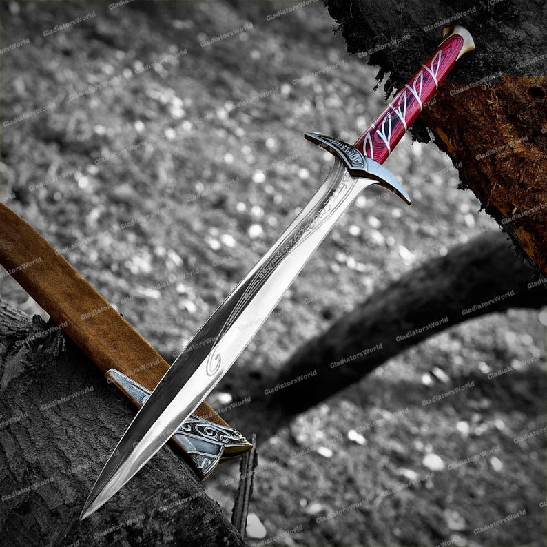 May include: A silver sword with a polished blade and a decorative hilt. The handle is red with white accents. The sword is resting on a wooden surface, with a brown sheath visible.