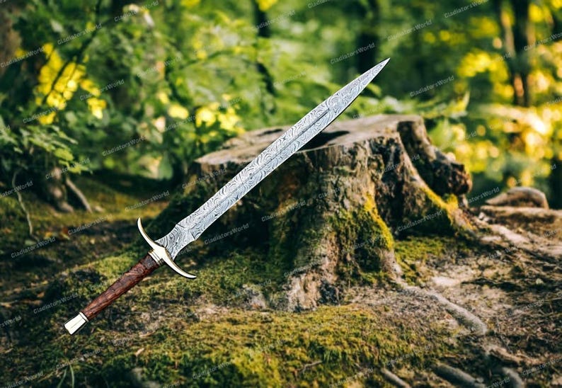 May include: A Damascus steel sword with a patterned blade, a brown wooden handle, and a gold-colored hilt. The sword is displayed outdoors, resting on a moss-covered tree stump, with a blurred green background.