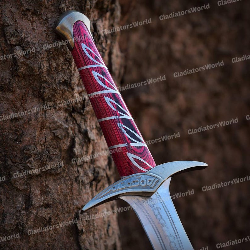 May include: Close-up of a sword with a red and silver handle. The handle has a decorative pattern and a silver pommel. The blade is silver with etched details. The sword is leaning against a brown tree trunk.