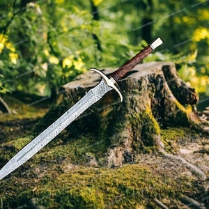 May include: A detailed, silver-colored sword with a patterned blade and a brown handle. The sword is resting on a moss-covered tree stump in a forest setting, with green foliage in the background.