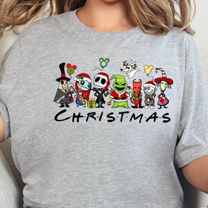 May include: A gray t-shirt with a graphic print of various cartoon characters from popular Christmas movies. The characters include Jack Skellington, Sally, Oogie Boogie, and the Grinch. The text "CHRISTMAS" is printed below the characters.