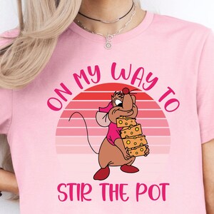 May include: A pink t-shirt with a cartoon mouse holding a stack of cheese. The shirt has a retro sunset graphic and the text "On my way to stir the pot".