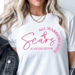 May include: White t-shirt with a pink ribbon and the text "All Warriors Have Scars #cancersurvivor" printed on the front.