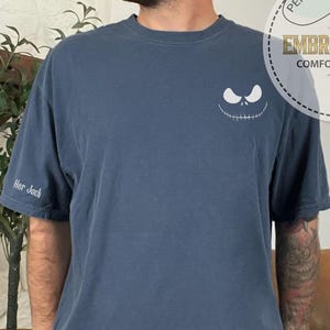 May include: A navy blue t-shirt with a white embroidered Jack Skellington face on the chest and "Her Jack" on the sleeve. The shirt also features a circular logo that says "Personalized Gift" and "Embroidered Comfort Colors".